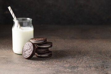 Wall Mural - Breakfast concept. Sandwich biscuits cookies filling with vanilla cream and  milk  jar on dark  concrete background