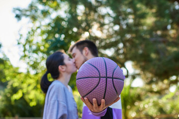 Violet basketball in the foreground, behind two young people kissing