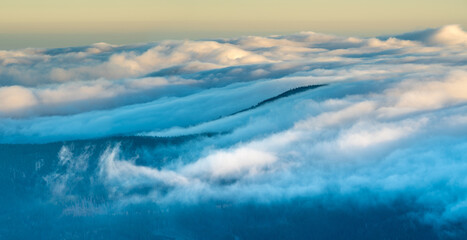 Wall Mural - waves of clouds rolling over the top of the mountain illuminated by the rising sun