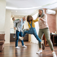 Happy caucasian family, grandparents and grandchildren having fun, playing and jumping on the floor in the living room