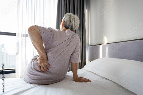 Stressed asian senior woman suffering from backache,sitting on bed massage her waist pain,unhappy old elderly people waking up in the morning after sleeping on uncomfortable mattress or bad posture