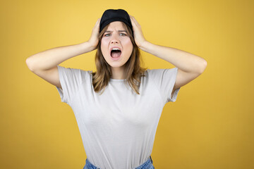 Beautiful young caucasian girl wearing french look with beret over isolated yellow background crazy and scared with hands on head, afraid and surprised of shock