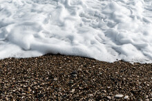 White Sea Foam On Multi-colored Pebbles. Close Up.