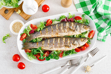 Seabass or sea bass fish roasted and fresh vegetable salad of tomatoes and lettuce, healthy food for lunch, top view