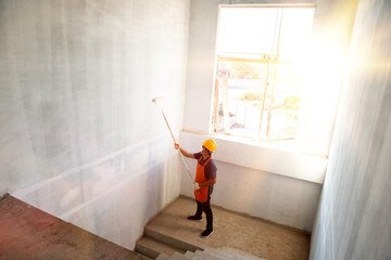 Wall Mural - Room paint job. Asian white room painter with a paint roller in a great hall on a construction site.