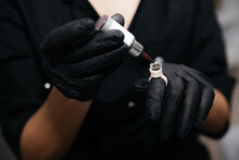 Permanent Makeup Artist Pours Brown Pigment Into The Paint Ring On Finger In A Black Glove. Close-up Of Pigment Container And Ink Bottle For Eyebrow Or Lip Tattoo. Beauty Procedure Preparation.