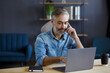 © YURII MASLAK - Senior grey-haired businessman talking on the phone in office. Conversation with business partners. Business portrait of handsome mature man sitting at workplace. Communication, negotiation.