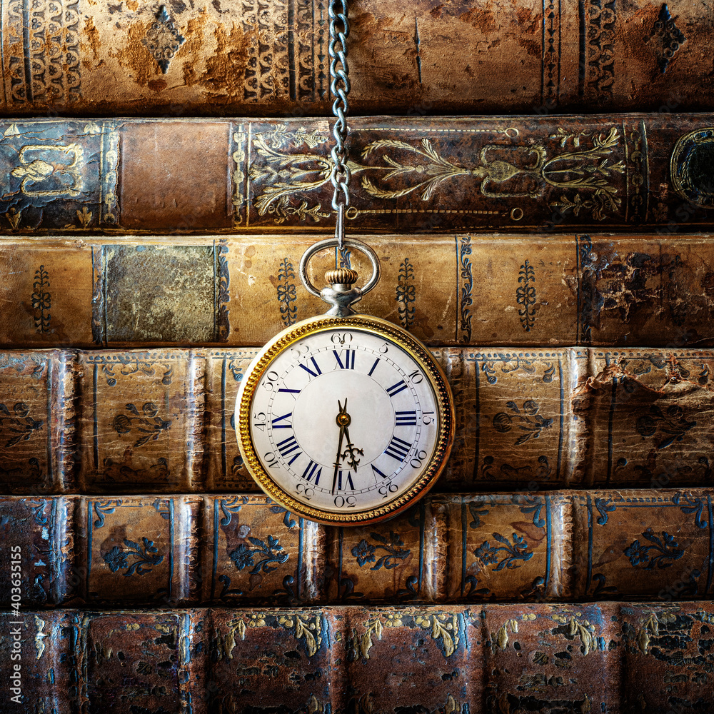 Vintage clock hanging on a chain on the background of old books. Old watch  as a symbol of passing time. Concept on the theme of history, nostalgia, old  age. Retro style. Stock, image size:1000x1000