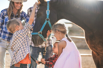 Wall Mural - Cheerful family enjoy day outdoor at ranch while the children cuddle a horse - Human and animal love