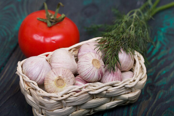 Wall Mural - Garlic in an overturned wicker basket. Dill sprigs and tomato. On green pine boards. Close-up shot.