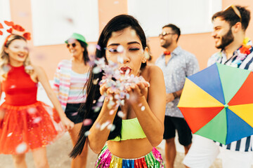 Wall Mural - Brazilian Carnival. Young woman enjoying the carnival party blowing confetti