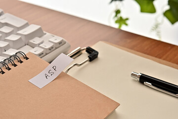Poster - A sticky note labeled ASP is taped to the edge of a notebook on the desk.That's an acronym for Application Service Provider.