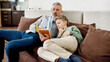 © Svitlana - Lets read a story. Grandfather reading a book with his little grandson while relaxing on sofa at home