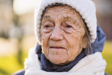 Outdoor portrait of senior woman in jacket , scarf and head wear in winter. Happy retirement. Joyful elderly person posing in the park in sunny cold weather. Happy mature woman enjoying walk in town