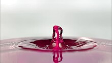 Water Splashing As Pink Droplet Falls Into Surface And Bounces Up In The Liquid.