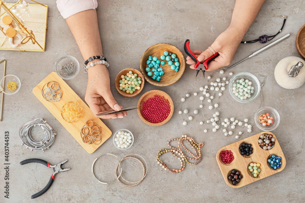 Female designer making jewelry on gray background