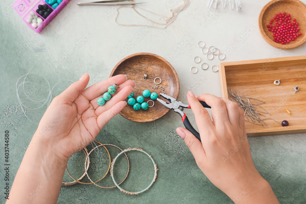 Female designer making jewelry on light background