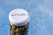 Jar of pickled capers with lid with expiration date on light blue table with copy space