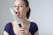 A young woman is licking at sharp kitchen knife 