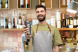 © Syda Productions - people, profession and job concept - happy smiling waiter in apron holding tumbler or takeaway thermo cup over bar background