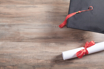 Graduation hat and diploma on the wooden background.