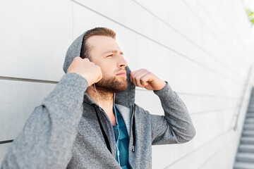 fitness, sport and lifestyle concept - young man in earphones listening to music outdoors