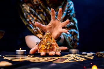 Sticker - The fortune teller holds a glass pyramid with gold in her hands and casts a spell over it. There are Tarot cards on the table. Close-up. The concept of divination, magic and esotericism