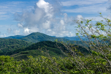 The landscape of the mountain ridge of Phuket and the Adaman Sea against the background of a blue sky with clouds.