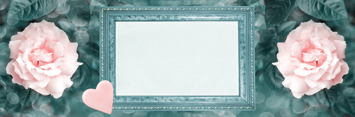 Frame with blank paper and a heart, on an unfocused widescreen background of blooming roses. Tinted image