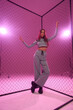 © Dmitry Tsvetkov - Young woman with long straight brunette hair in sporty clothes standing against grid fence and pink background. Full length fashion portrait