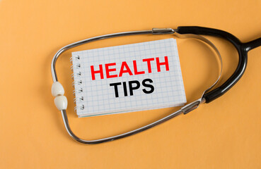 Text Health Tips on a notepad with a stethoscope lying on a orange background