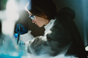 Female vaccine researcher in laboratory coat, protective goggles and gloves transfers chemical solution to test tube. Scientists worldwide endeavor to develop anti-coronavirus vaccine or treatment