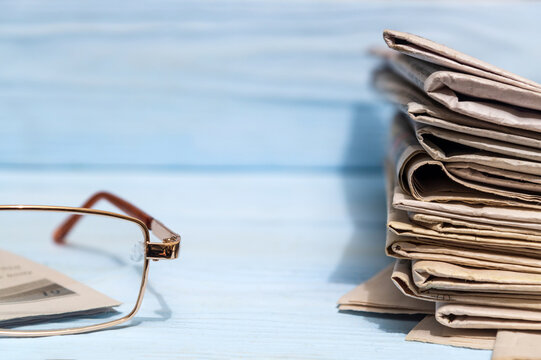 Reading glasses and stack of newspapers on a blue wooden shelf