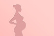 Silhouette of a pregnant woman on a pink background. The concept of the birth of a child. The girl with the belly. The duration of pregnancy. Waiting for the birth of a baby. Mother. Gestation of the 