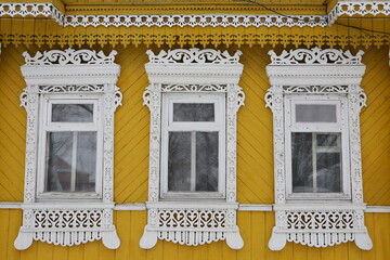 Ornamental windows with carved frames on vintage yellow wooden rural house in Dunilovo village, Ivanovo region, Russia. Building facade. Russian traditional national folk style in wooden architecture