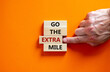 Go the extra mile symbol. Wooden blocks with words 'Go the extra mile'. Male hand. Beautiful orange background. Business and go the extra mile concept. Copy space.