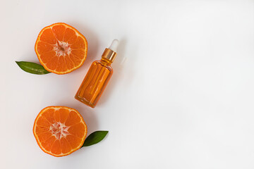 A bottle of aromatic tangerine oil and two halves of a cut tangerine on a white background with space for text, top view.