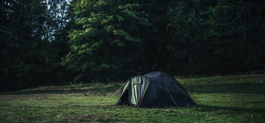 Wall Mural - Black tent in the middle of a field on the background of green trees