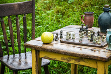 Old Chess Board And Green Apple On Old Wooden Table And Chair In Rain