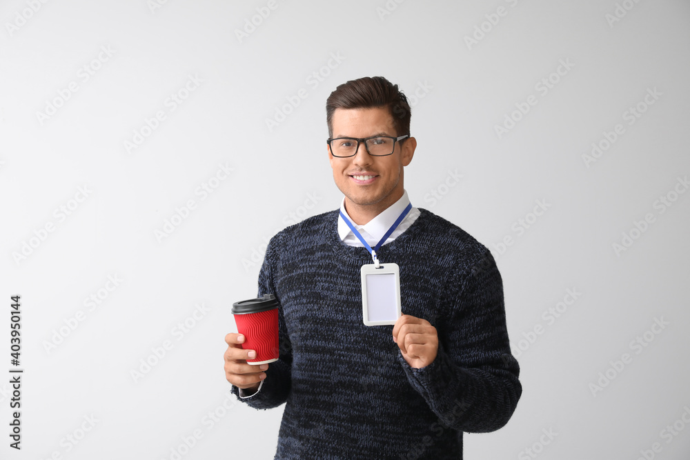 Young man with blank badge and takeaway cup on white background