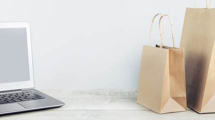 Laptop mockup with buff paper shopping carry bags on grey. online delivery service of goods and grocery, internet shopping. Environment and eco friendly packaging, plastic free takeaway. lockdown