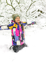 Happy little girl on a walk in a winter park in snowfall from trees.