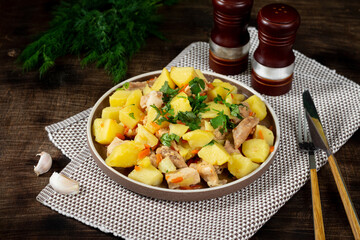 Stewed potatoes with meat. Roast potatoes with pig meat on a ceramic plate on a brown table. Roast meat