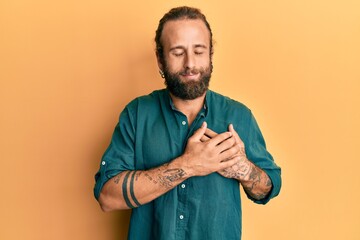 Handsome man with beard and long hair wearing casual clothes smiling with hands on chest, eyes closed with grateful gesture on face. health concept.