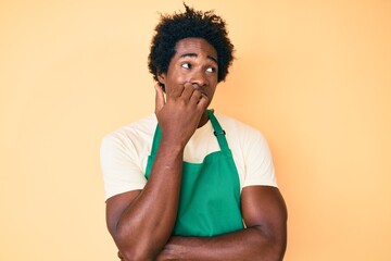 Poster - Handsome african american man with afro hair wearing waiter apron looking stressed and nervous with hands on mouth biting nails. anxiety problem.