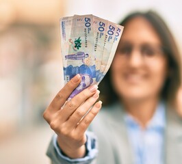 Wall Mural - Young hispanic businesswoman smiling happy holding colombian 50 pesos banknotes at the city.