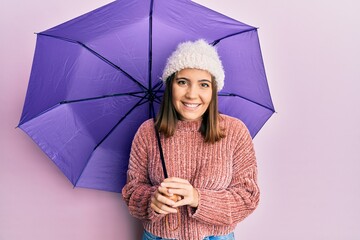 Poster - Young beautiful woman holding purple umbrella looking positive and happy standing and smiling with a confident smile showing teeth