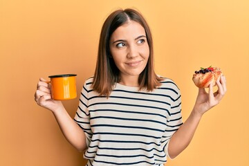 Poster - Young beautiful woman drinking coffee and eating pastry smiling looking to the side and staring away thinking.