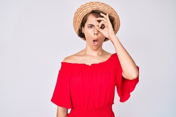 Sticker - Young hispanic woman wearing summer hat doing ok gesture shocked with surprised face, eye looking through fingers. unbelieving expression.