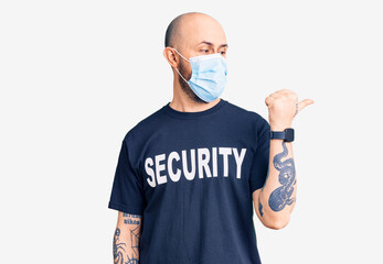 Wall Mural - Young handsome man wearing security t shirt and medical mask smiling with happy face looking and pointing to the side with thumb up.